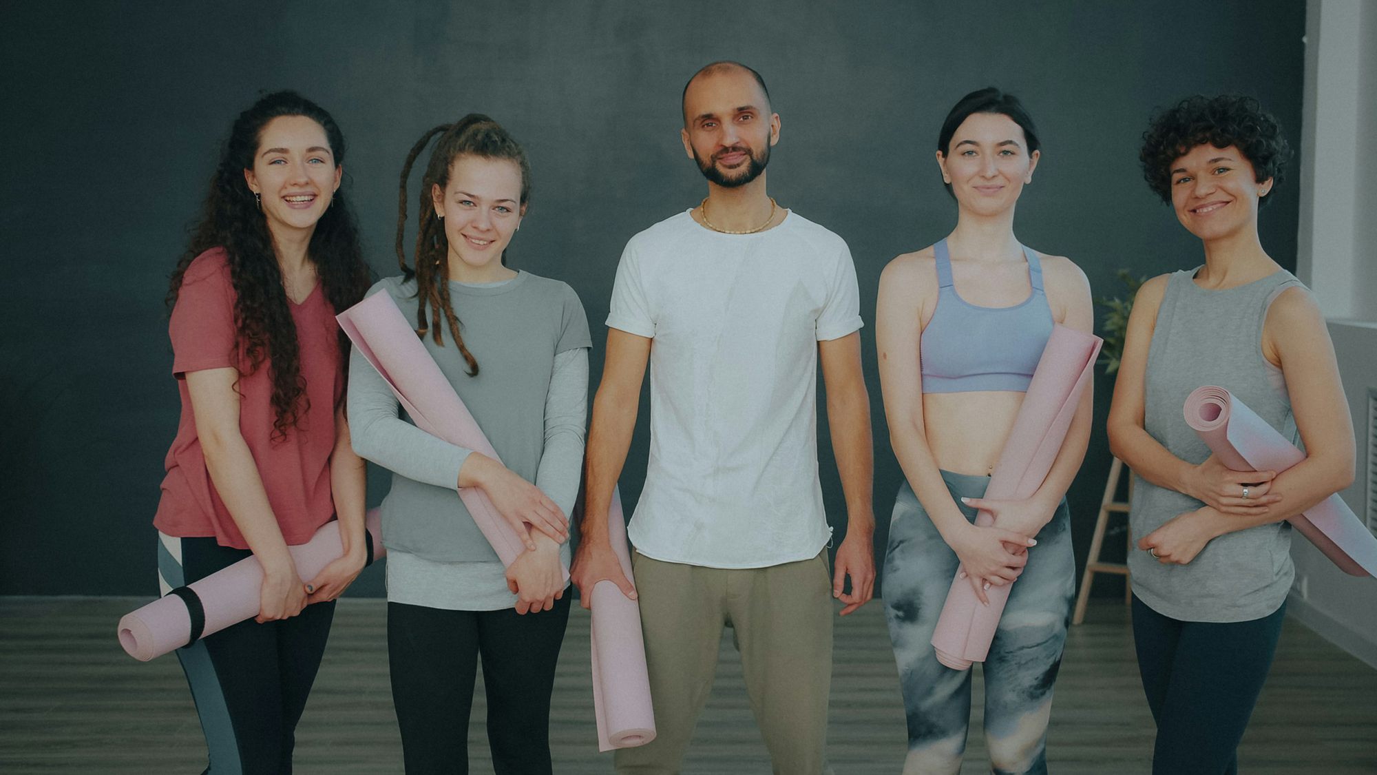 Five people from the studio standing in a row holding rolled mats