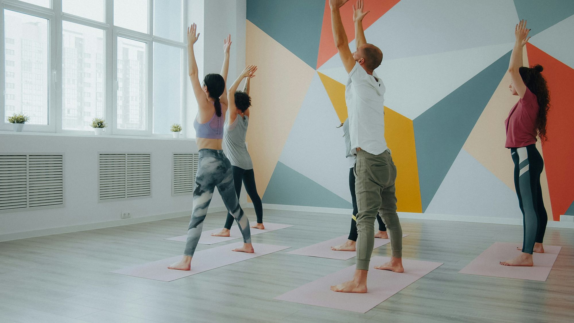 The studio: tall windows, a coral, orange and slate mural, and a class on pink mats