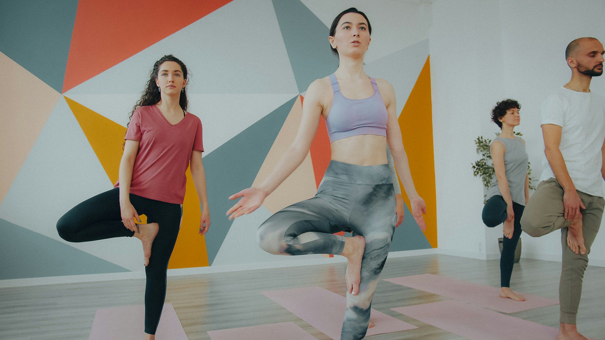 A class balancing on one leg in front of the coral and orange mural