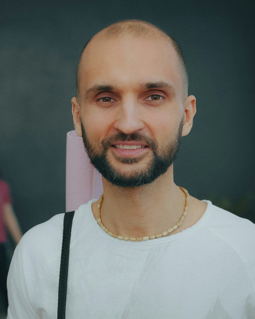 Sami, shaved head and a beard, in a white t-shirt, smiling
