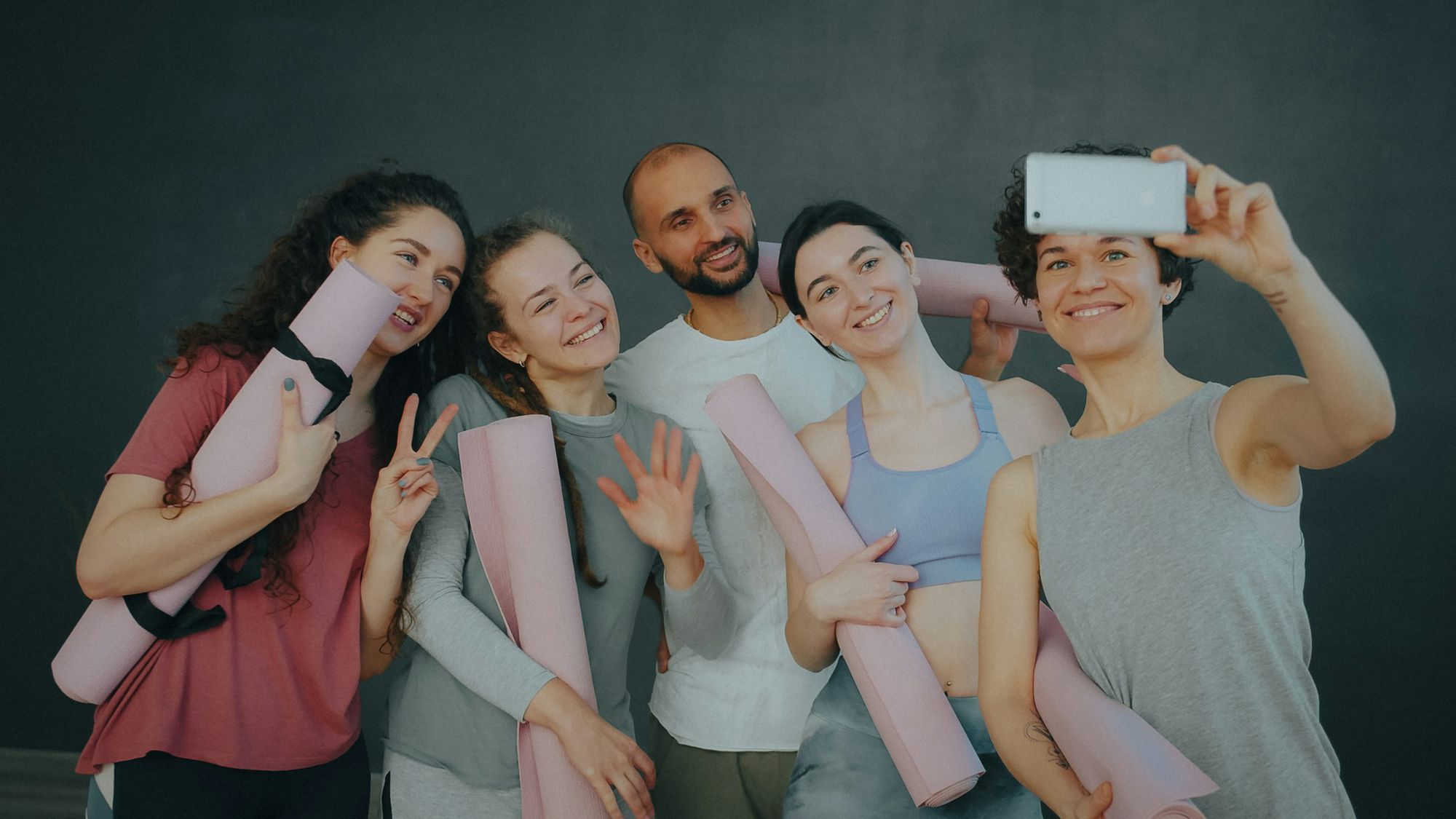 Five people from a class squeezed together for a selfie, holding their mats