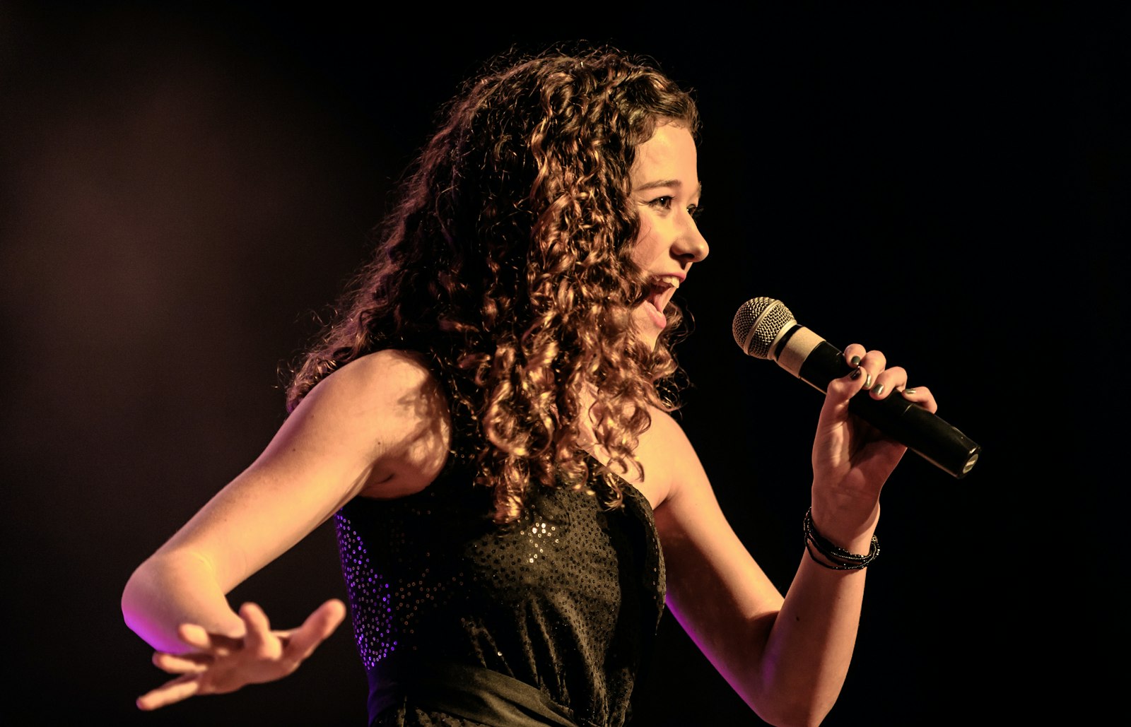A young singer performing at the school recital under warm stage lights