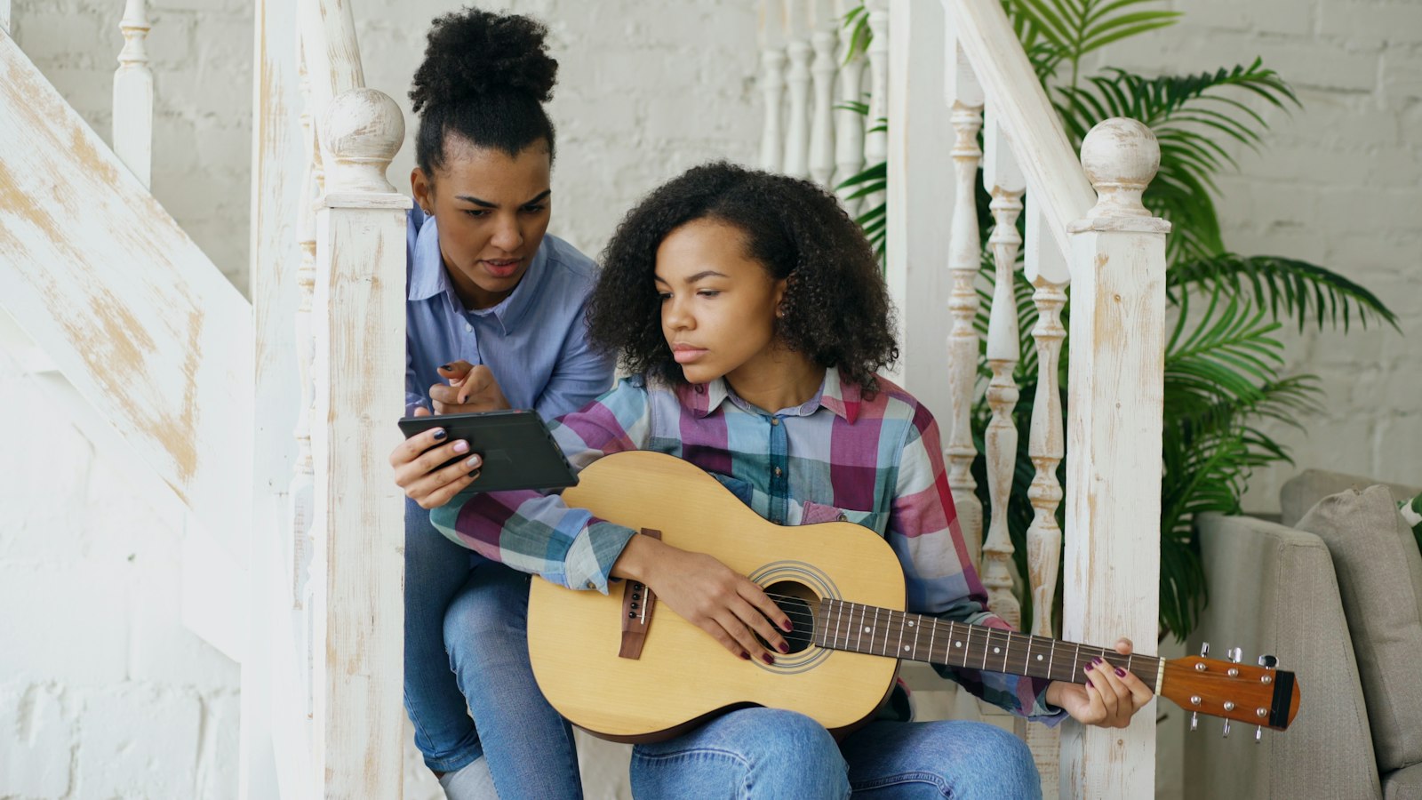 A teenager learning guitar on the stairs with her teacher