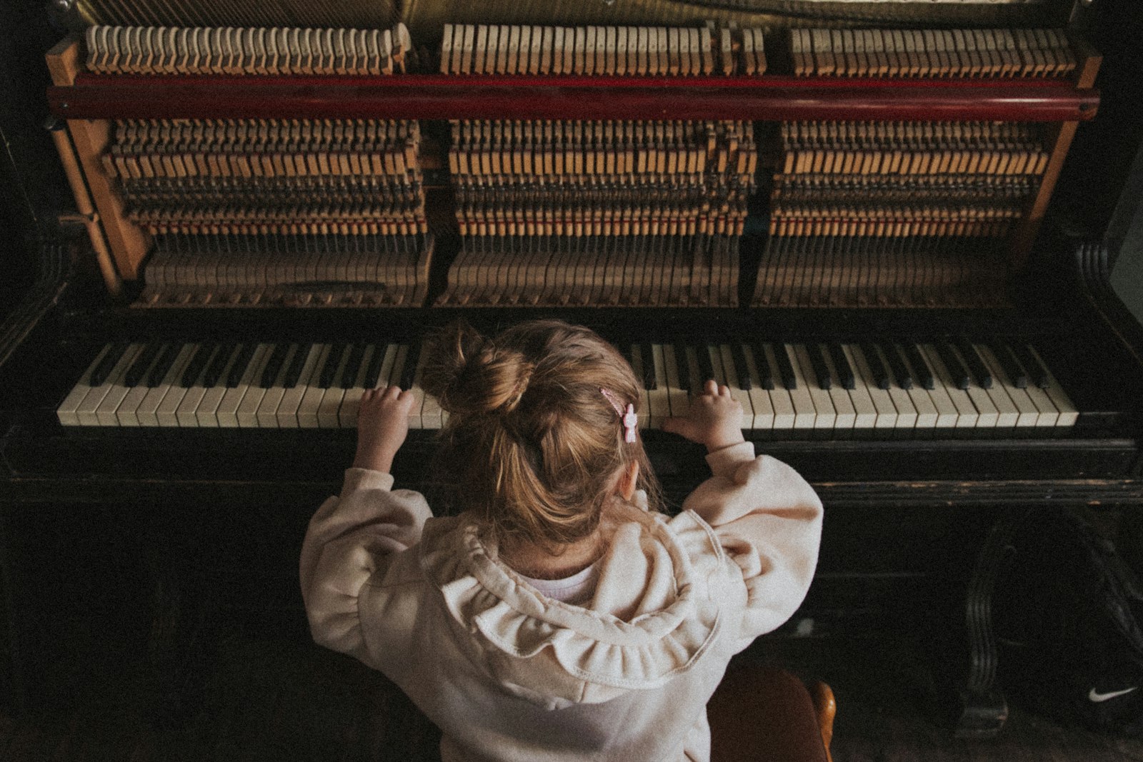 A toddler reaching up to the keys of an upright piano