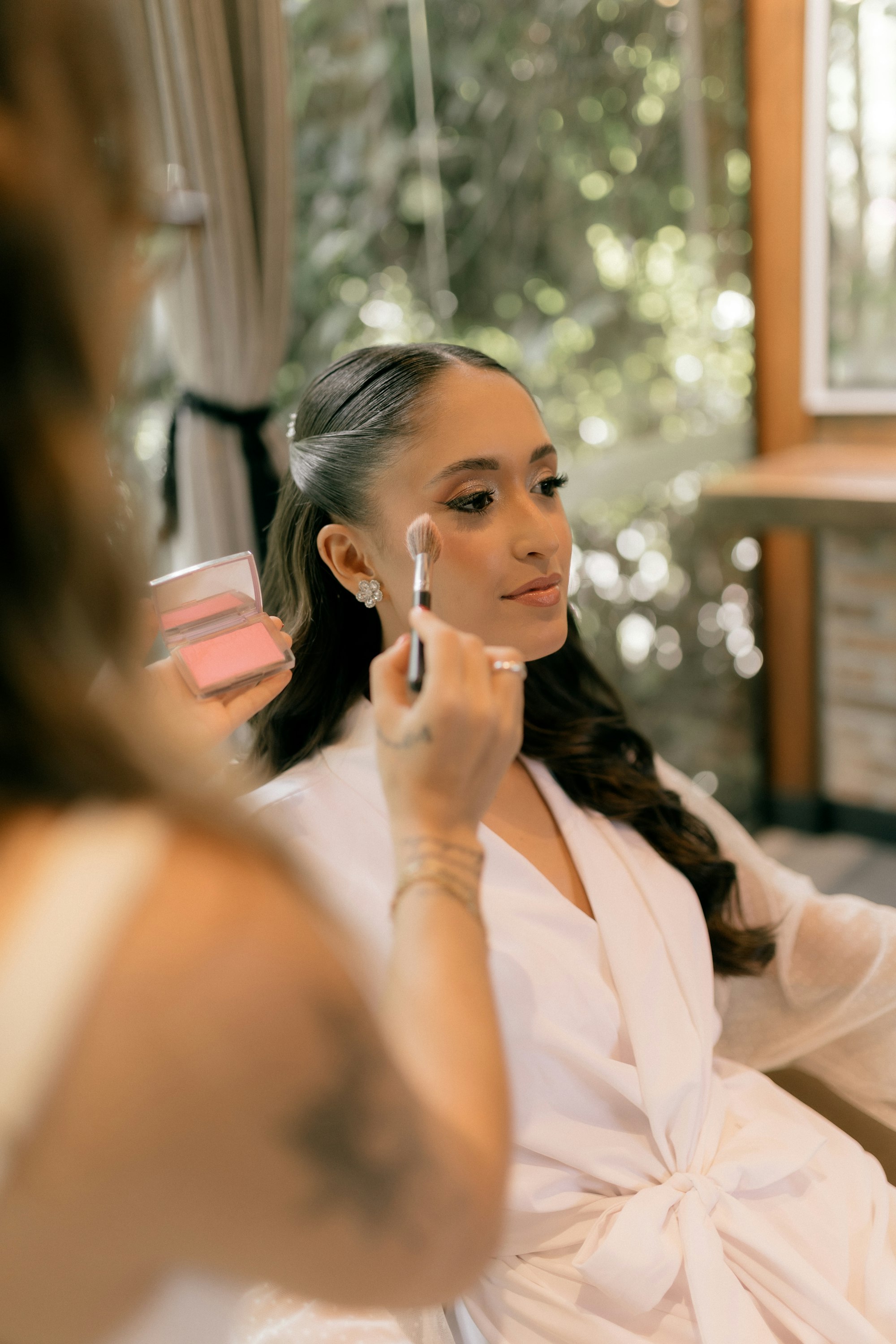 Marisol brushing blush on a bride in a white robe