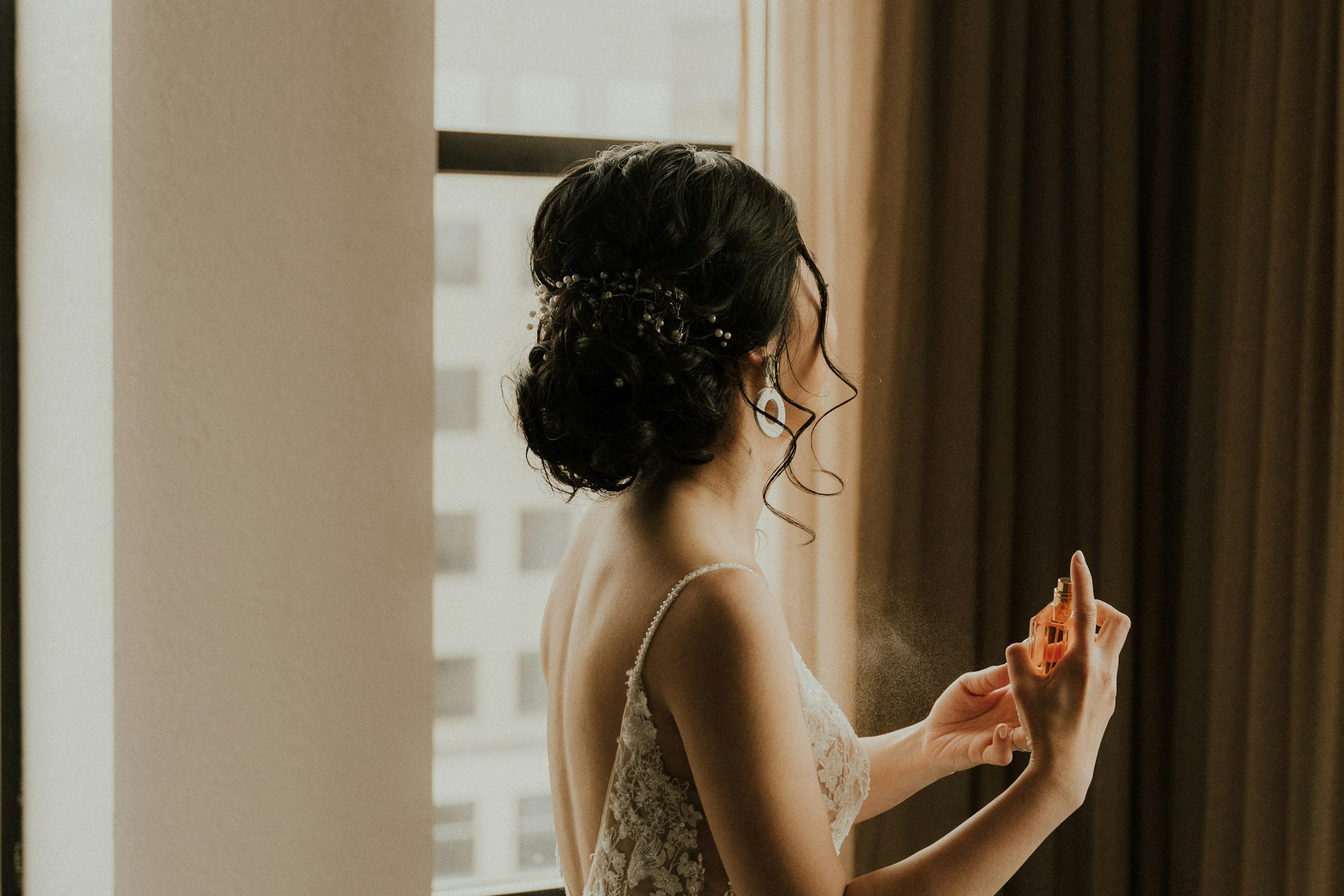 A bride by the window, hair pinned, a last spray of perfume before the first look