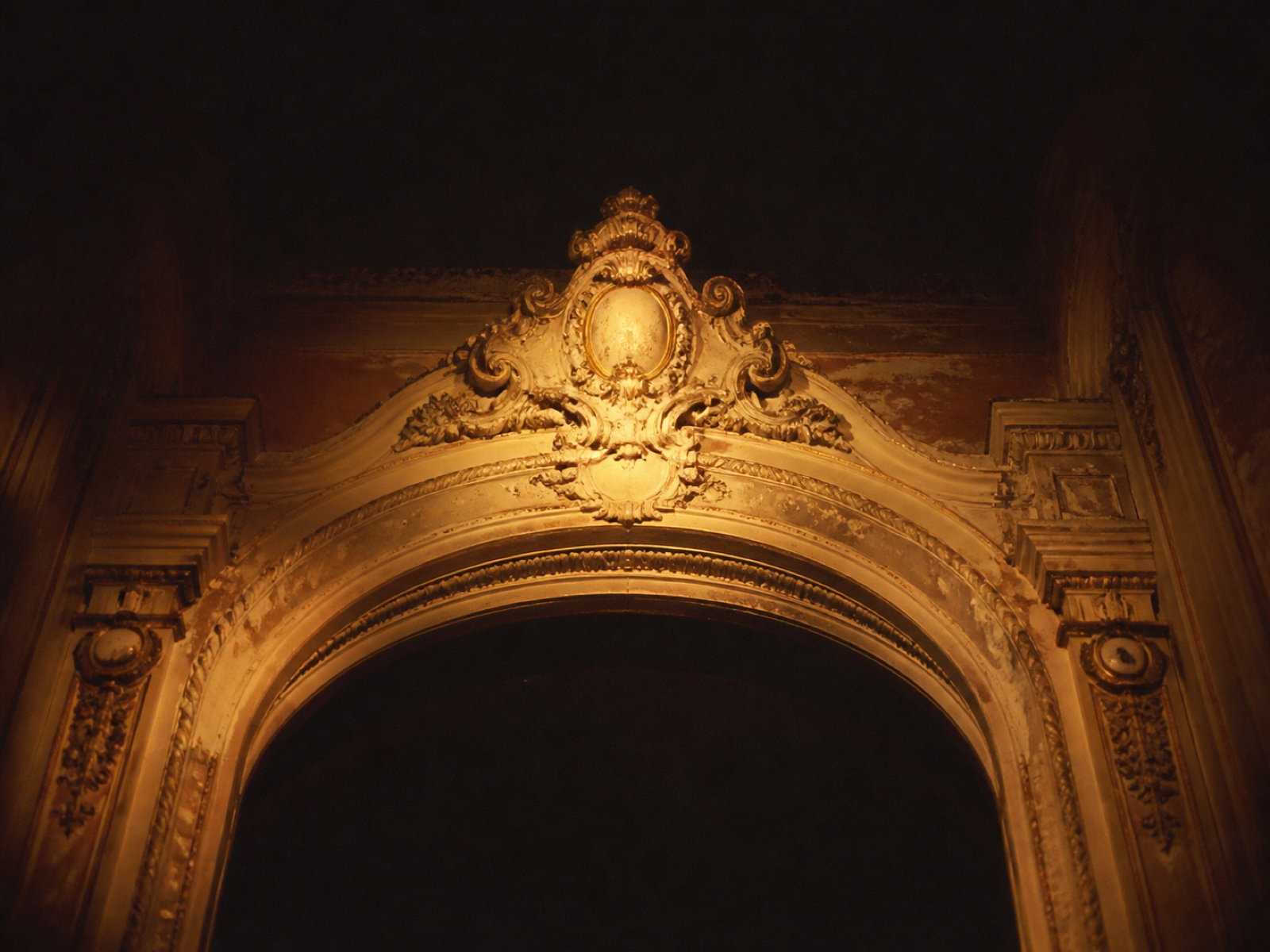 The theatre's ornate plaster proscenium arch photographed from the stalls, gilt detail catching a single warm work light