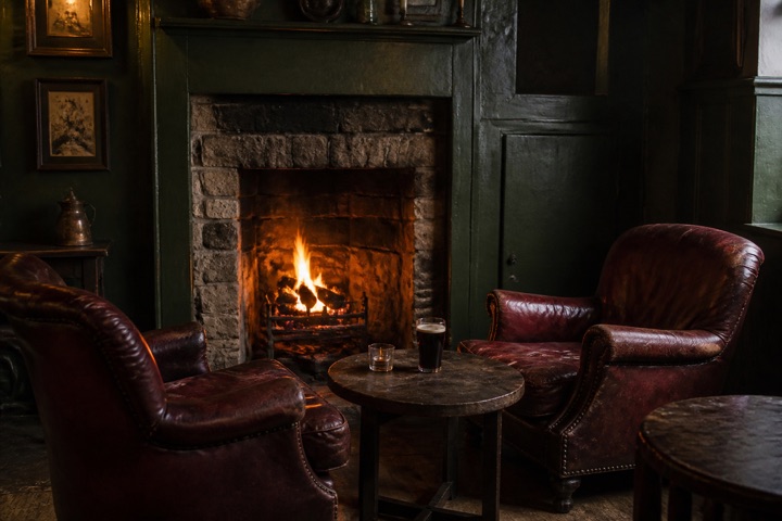 The snug fireplace surrounded by worn leather armchairs