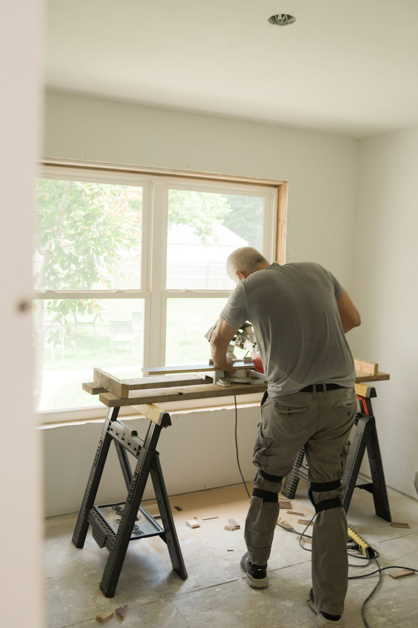 A carpenter cutting trim on a sawhorse in a client’s sunlit front room