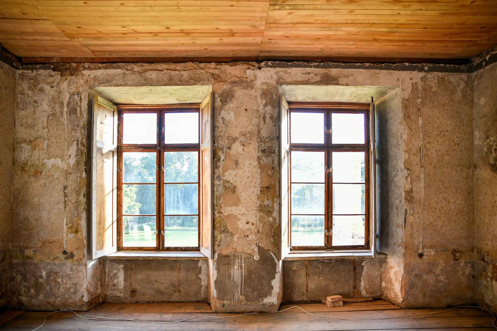 An old room stripped to bare plaster and lath between two tall windows