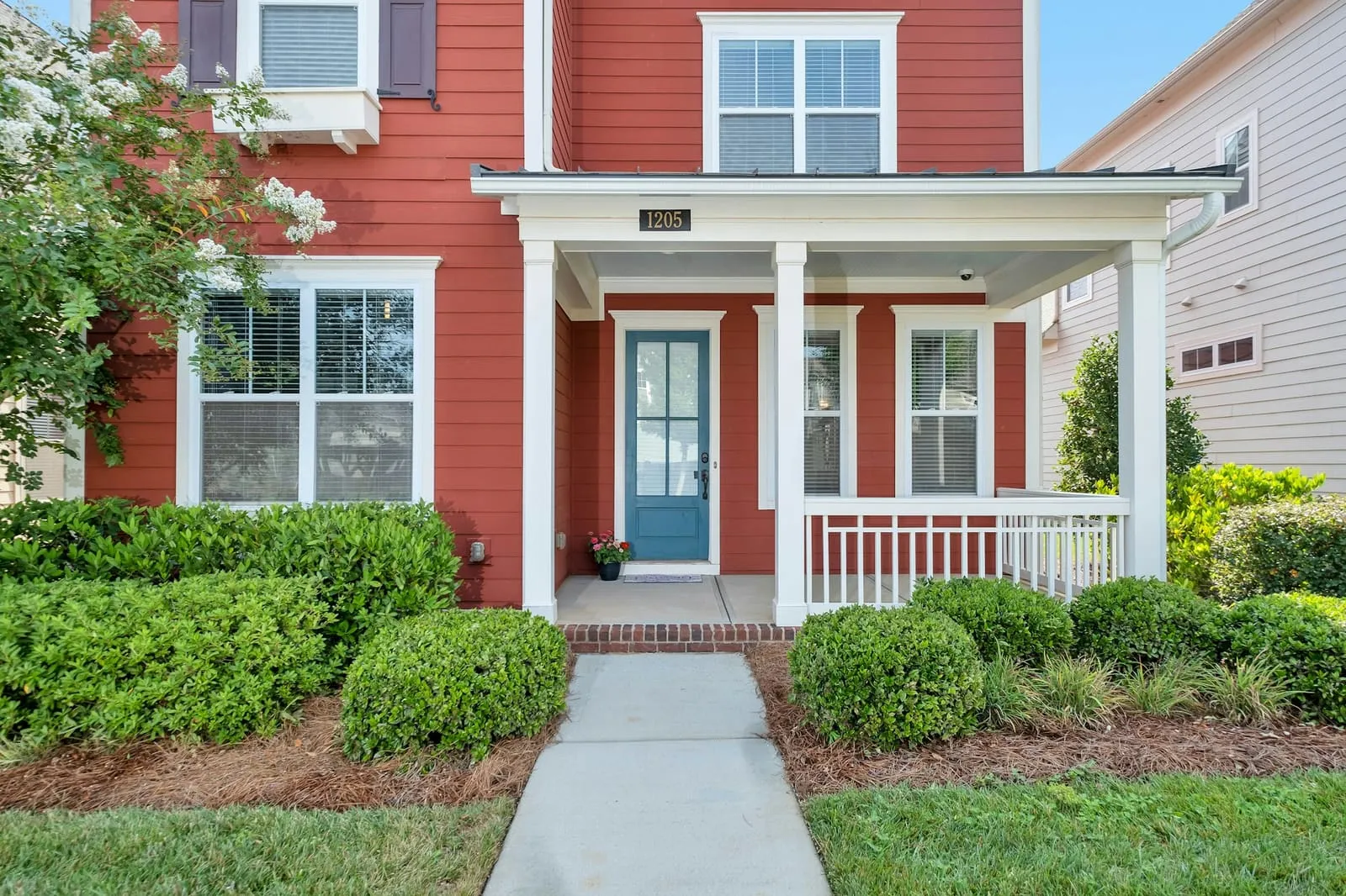 A red two-story frame house with a white front porch and boxwood hedges