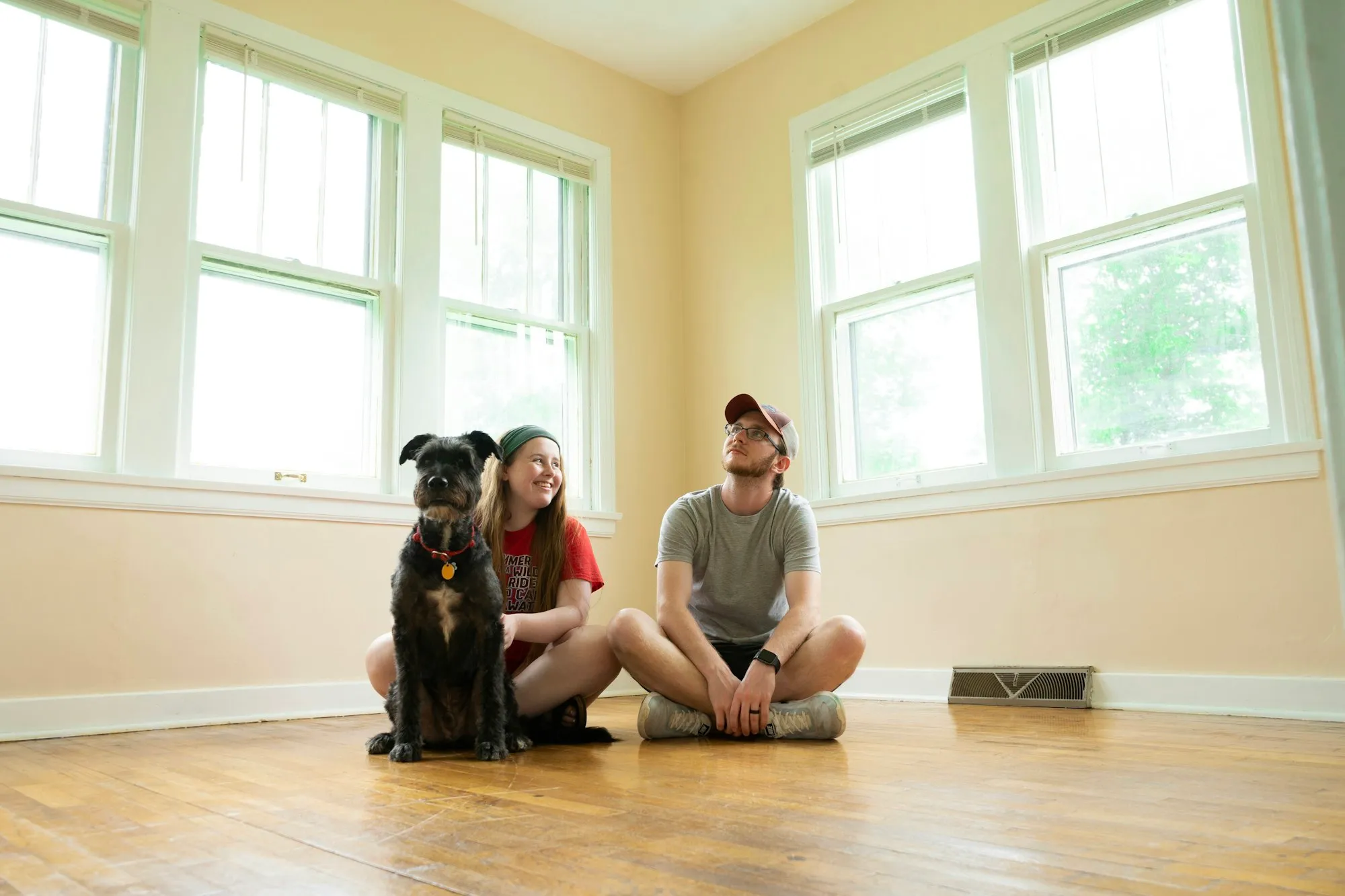 A couple and their dog sitting on the floor of their empty new living room