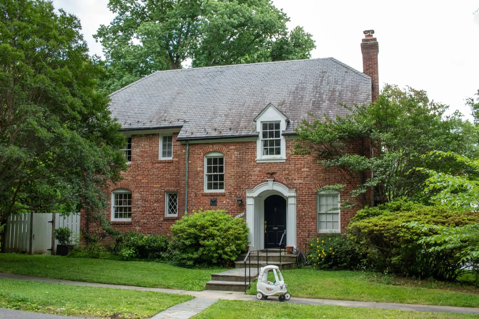 A brick colonial with dormers behind clipped shrubs