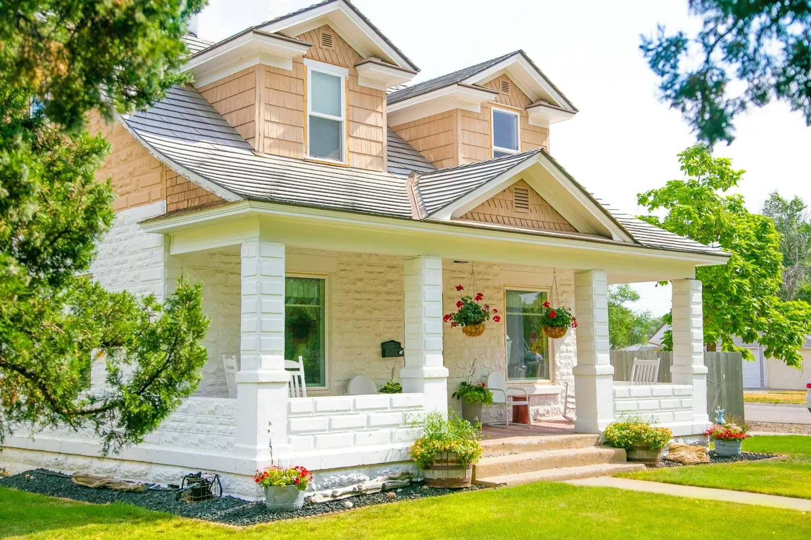 A craftsman house with a deep white porch and hanging ferns