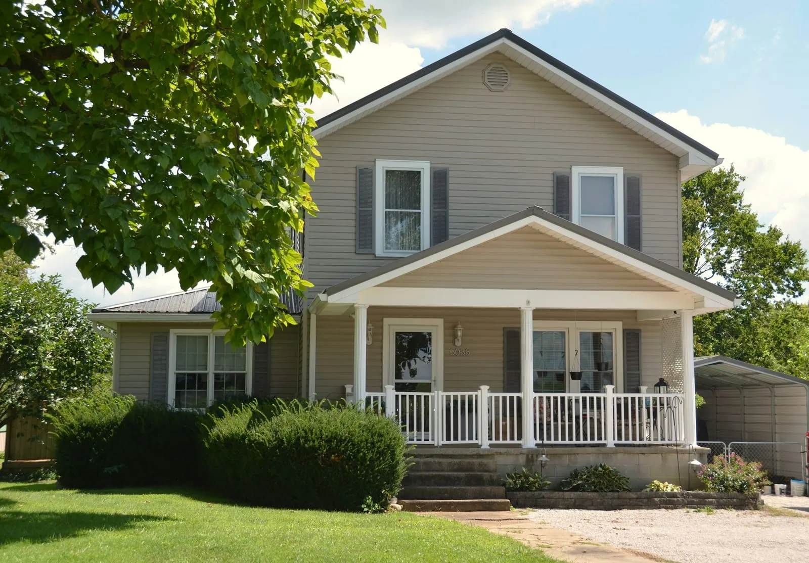 A gray frame house with a white porch on a quiet street