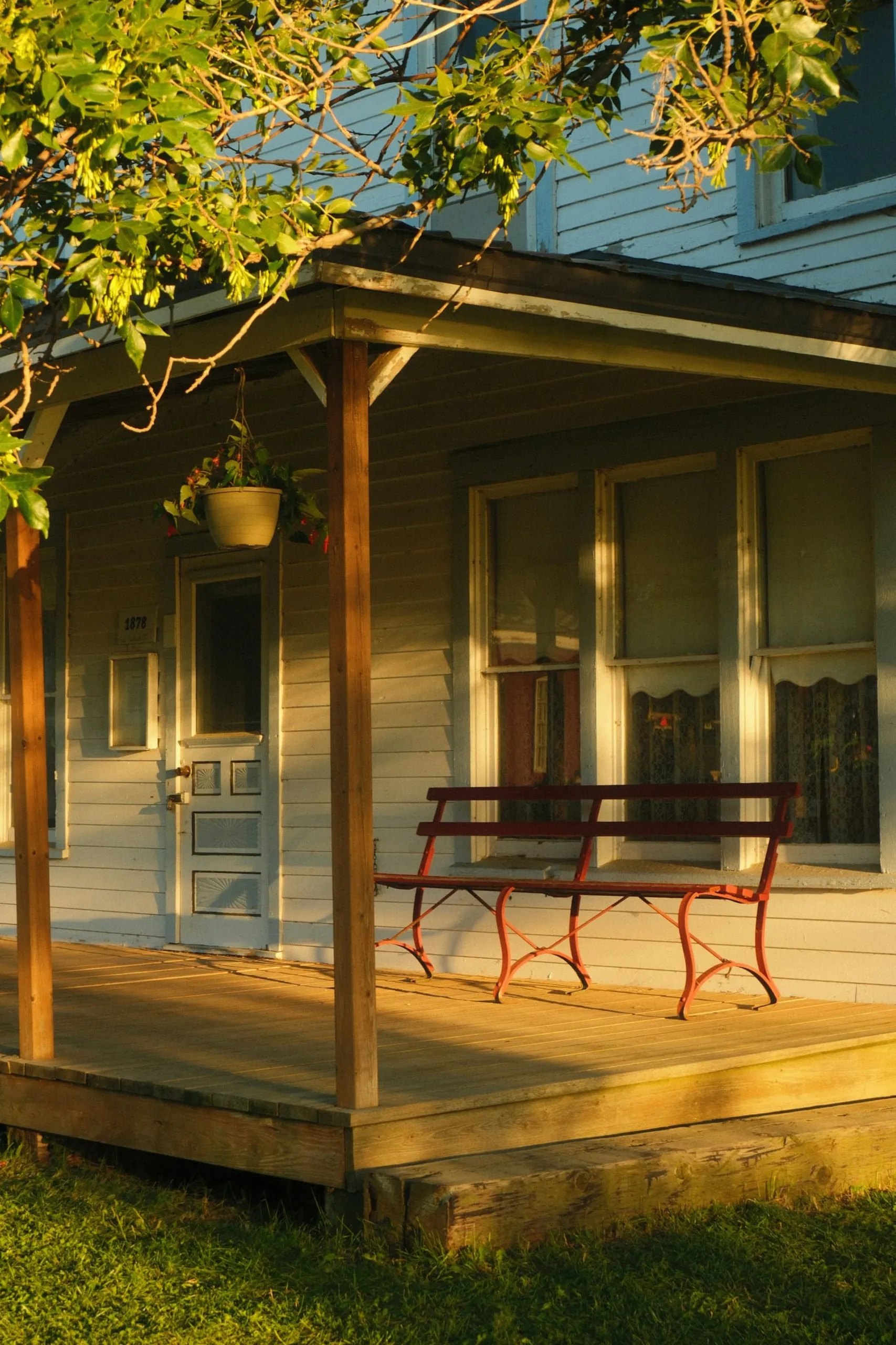 An old wooden porch with a red bench under a hanging fern
