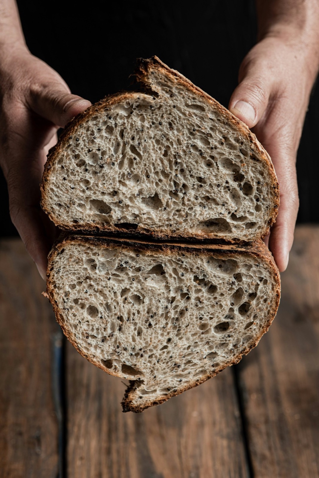 A halved loaf of seeded rye showing a dense dark crumb