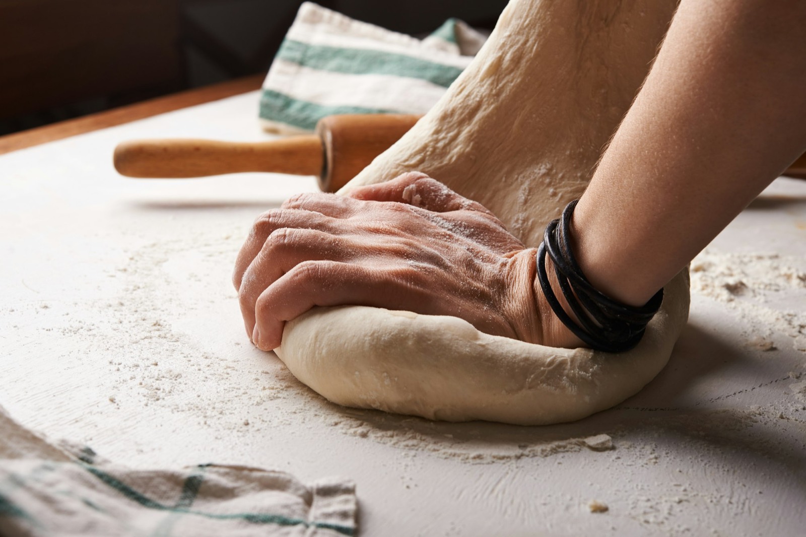 Hands folding a soft dough on a floured bench