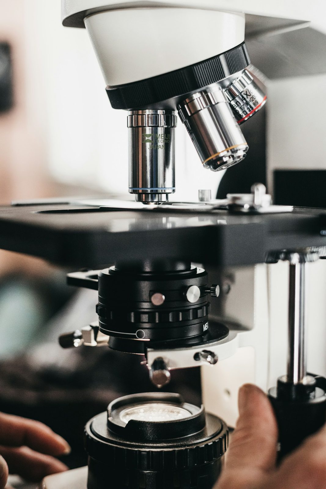 A student's hand focusing a microscope
