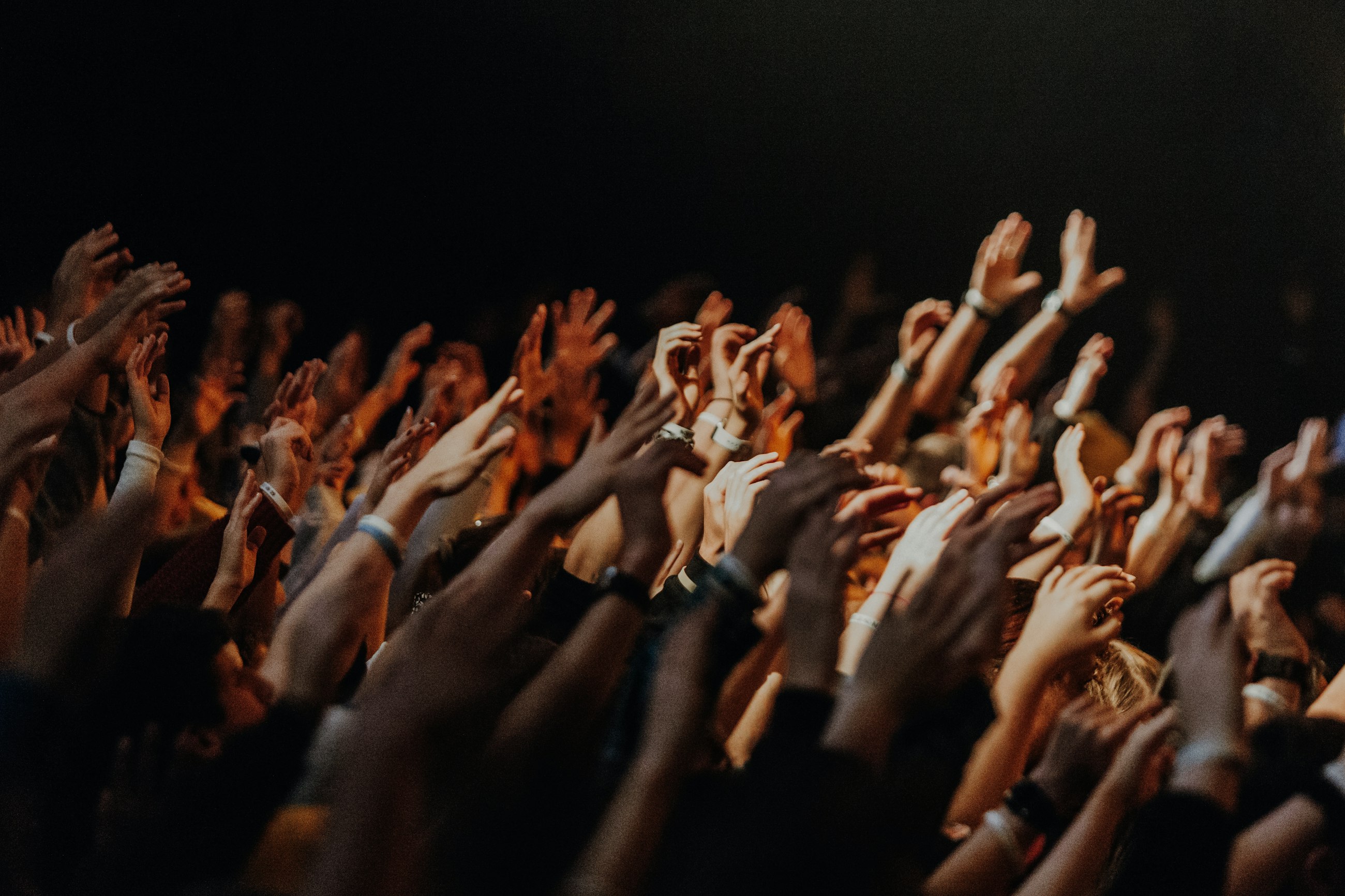A room full of people with their hands raised towards the stage, lit warm from the front.