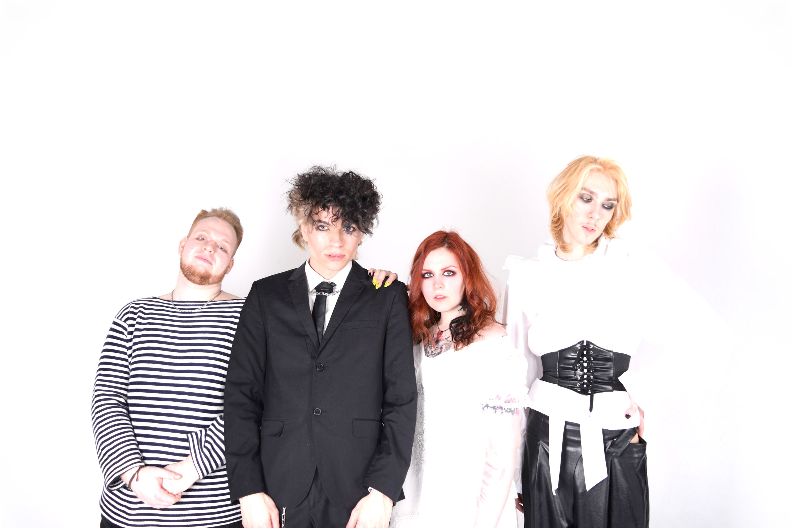 Lacemaker, four people standing in a white studio: Tom in a striped top, Sol in a black suit, Ivy in a white lace dress, Bea in a ruffled shirt and corset.