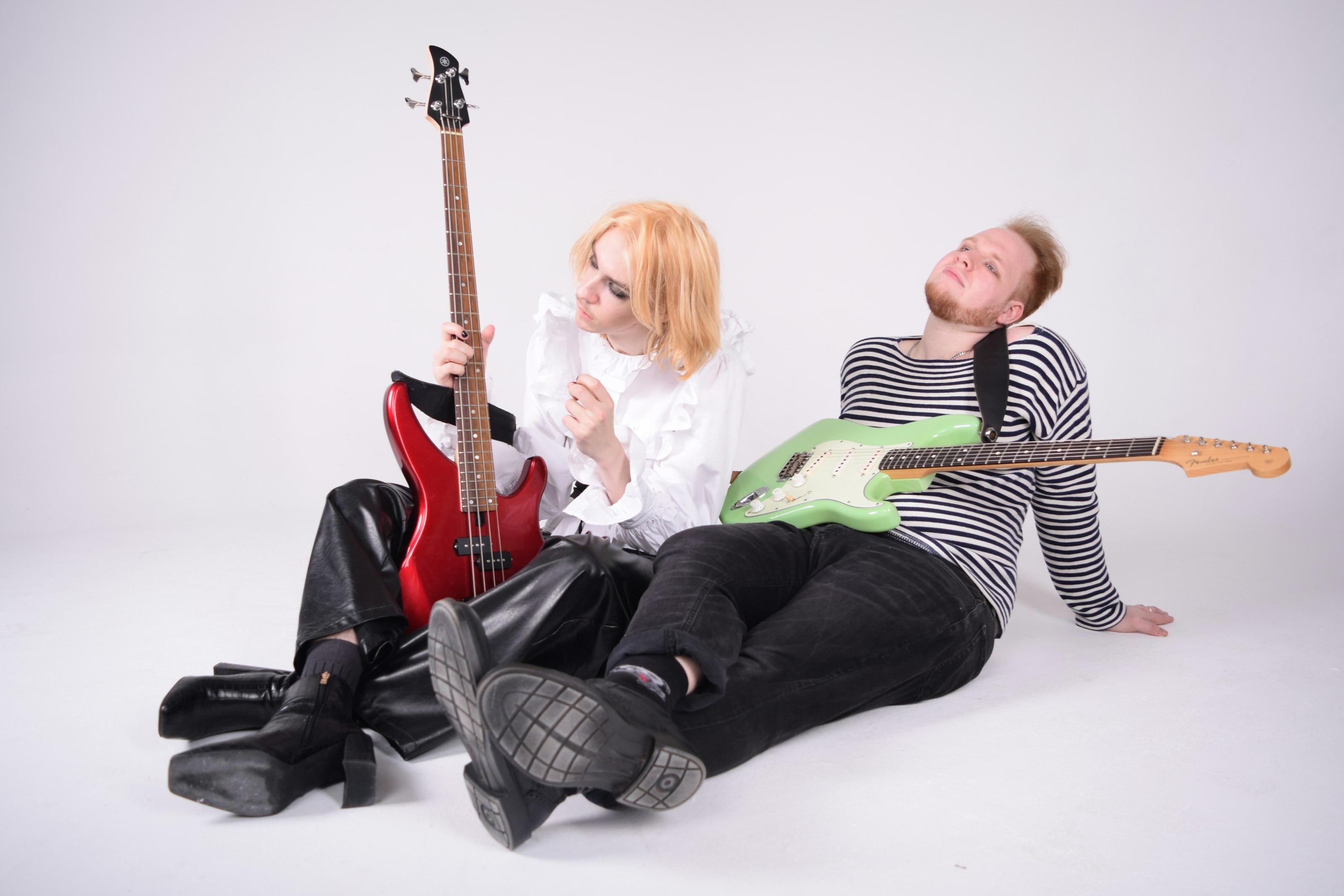 Bea and Tom sitting on a white floor with the red bass and the green guitar.