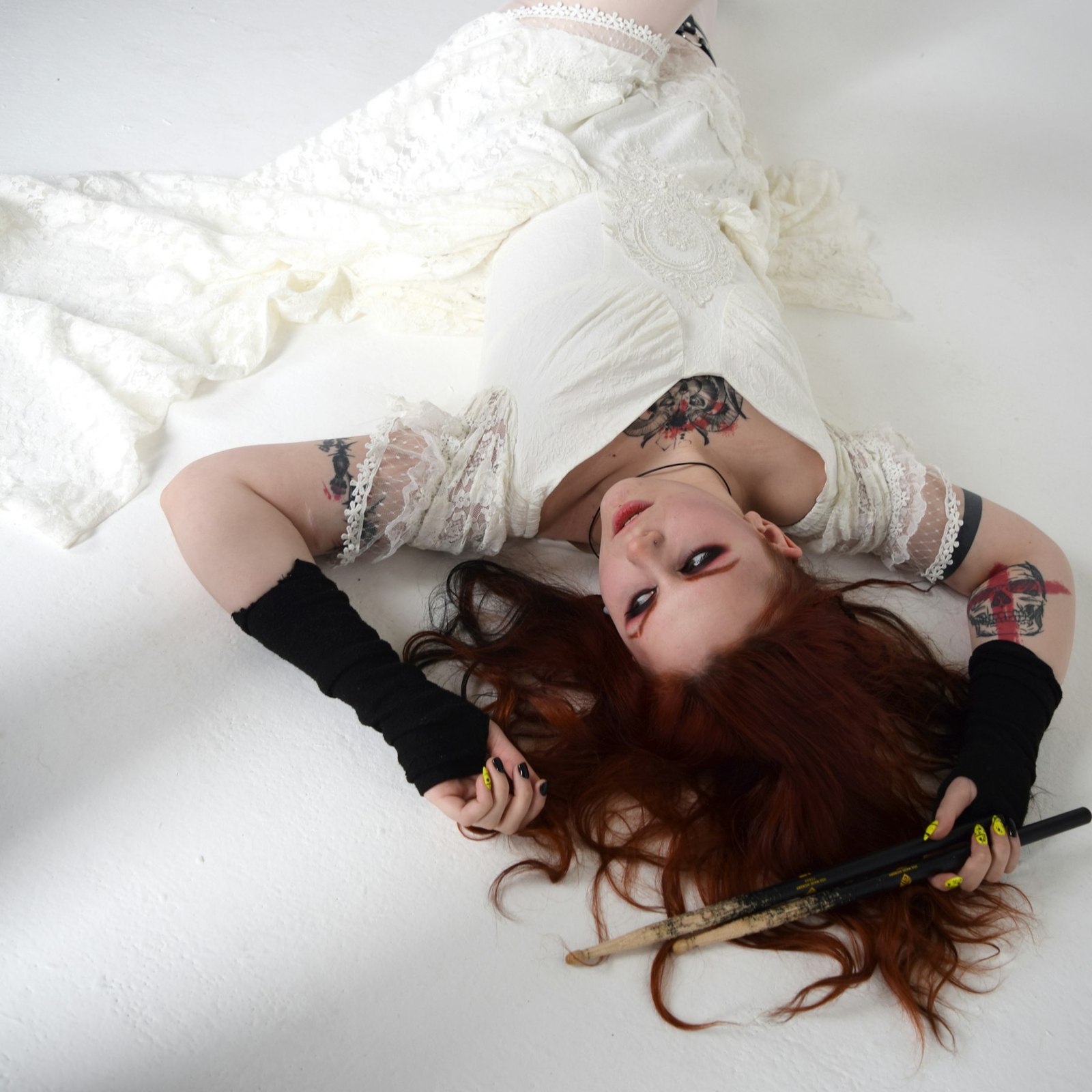 The cover of Cluny: Ivy lying on a white floor in a lace dress, her red hair spread out, drumsticks in her hand.